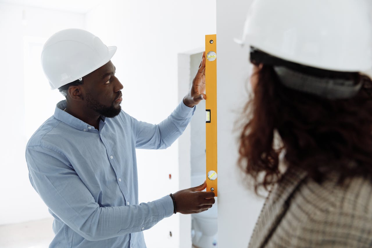 An adult man in safety gear uses a spirit level indoors for accurate measurements.